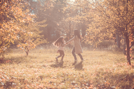 Mum and daughter playing in golden autumn garden. Nature concept.の写真素材