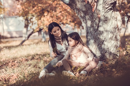 Mum and daughter in autumn garden. Sitting under tree and talking.の写真素材