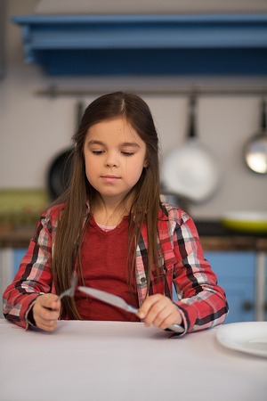 Close up of little nice girl holding cutlery. Standing at table.の写真素材