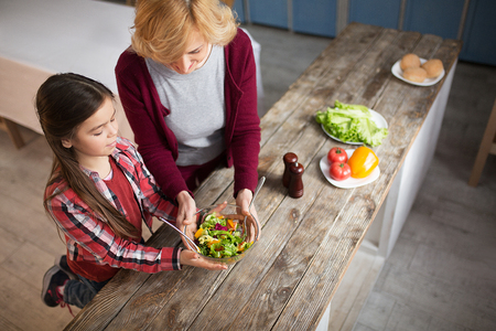 Up view image of grandma and granddaughter holding bowl with salad. Two spoons in bowl.の写真素材