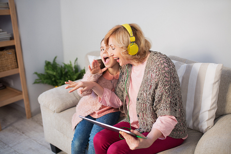 Granny and granddaughter listening music at home. Sitting on sofa.の写真素材