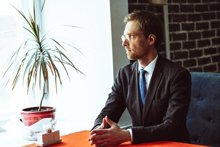 Confident businessman sitting at restaurant and looking aside. Thinking about future agreement.の写真素材