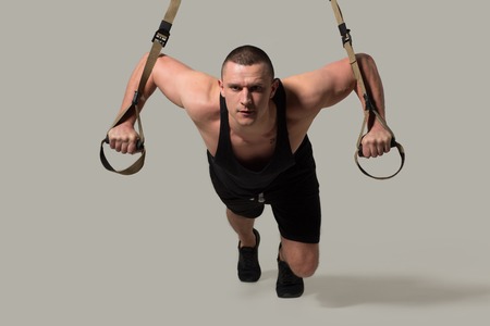Close up image of fit sportsman training on modern TRX bodybuilder. Sport equipment concept.