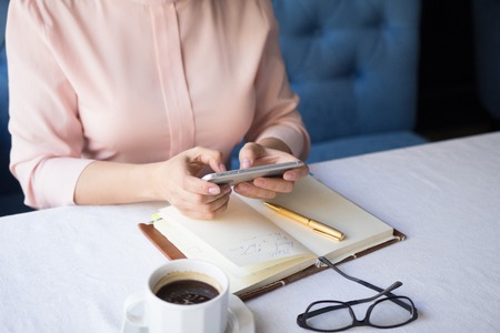 Business woman texting on her mobile phone while sitting at table.の写真素材