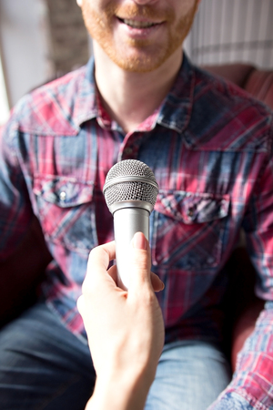 Guy talking into microphone smiling close cropped portrait. Cropped picture of man wearing denim shirt speaking in mic taken from operators view.の写真素材
