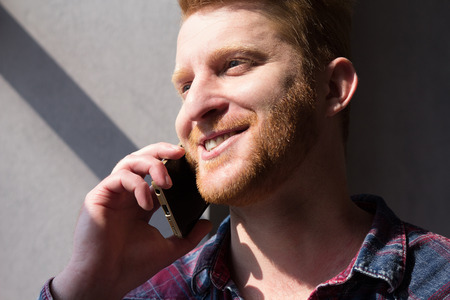 Good looking boy having conversation over phone smiling. Gorgeous man smiling while talking on his cell phone with sun shining all over his face.の写真素材