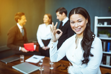 Smiling asian business woman showing OK sign after profitable meeting.の写真素材