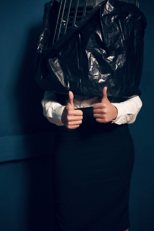 Crazy girl with garbage can on her head. Woman wearing white shirt blouse and formal black heels standing still in corner with trash can covering half of her body.の写真素材