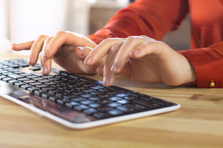 Womans hands on pc wireless keyboard. Gentle female hands with nude manicure slightly lifted above keyboard in process of typing.の写真素材