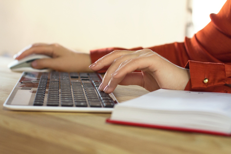 Close up shot of businesswomans hand on keyboard. Woman hands typing on pc wireless keyboard at wooden office table with notebook lying next to her.の写真素材
