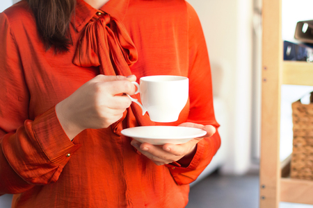 Gentle female hands hold small porcelain tea sized cup and plate. Cropped picture of pretty woman standing and enjoying her coffee in little white cup.の写真素材
