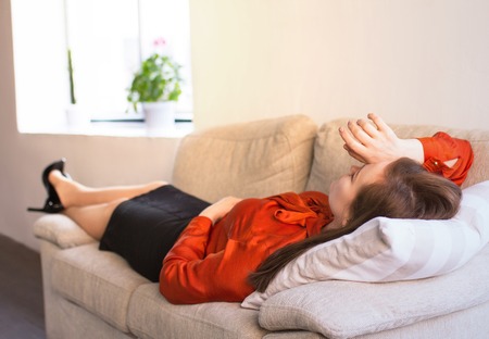 Overworked business lady resting on sofa. Tired businesswoman lays asleep on couch at home after long day at work with her hand at her forehead.の写真素材