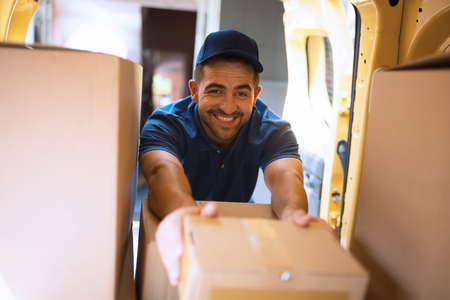 Delivery man get packages out of car. Delivery guy smiling wide while reaching for package to take out from back of his mini van.の写真素材