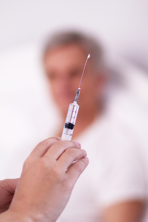 Nurse holding injection in her hands. Close up shot of female doctors hands holding syringe. Patient blurred in background.の写真素材
