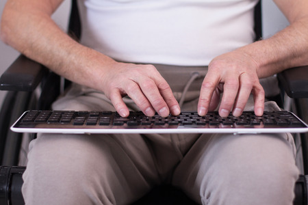Front view of man in wheelchair typing on keyboard. Senior man sitting in his wheelchair and working on wired keyboard on his lap.sの写真素材