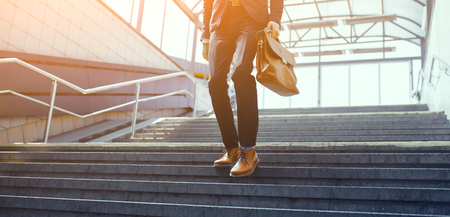 Man in suit walking down stairs. Formaly dressed guy making his way down concrete staircase with brown leather bag in his hand.の写真素材
