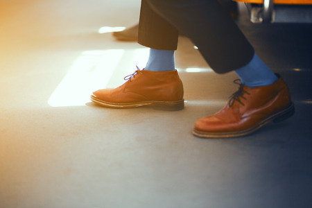 Businessmans shoes. Elegant brown leather shoes and blue socks worn by businessman on subway train.の写真素材