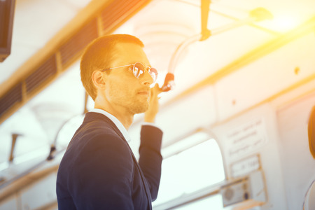 Handsome businessman standing in subaway train. Good looking guy wearing suit and round sunglasses standing in metro holding on to metal bar.の写真素材
