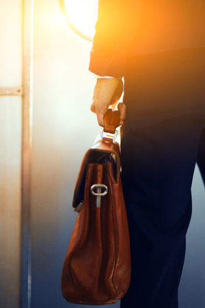 Brown leather case in hands of man. Cropped picture of businessman in suit standing in subway train and holding brown bag in his hand.の写真素材