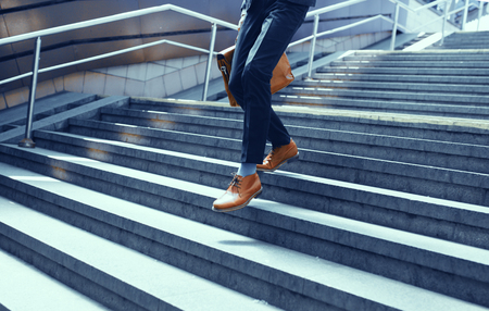 Cropped picture of guy in suit walking down stairs. Businessman dressed in suit and leather shoes walking down concrete steps.の写真素材