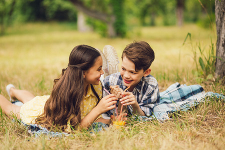 Two little kids having picnic together outside. Happy smiling boy and girl lying together on rug and having beverage from straw.の写真素材