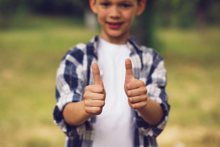 Adorable little boy showing thumbs up. Cute smiling boy wearing white and blue button up and white shirt underneath showing thumbs up with both of his hands.の写真素材