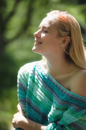 Gorgeous lady with sun shining on her face. Portrait of beautiful woman covered in sunshine wearing knitted jumper outside in nature.の写真素材