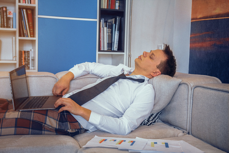 Young handsome man with laptop sleeping on the sofa. Fall asleep while working.の写真素材