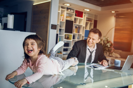Little daughter playing with father while he he going to work on laptop. Business at home concept.の写真素材