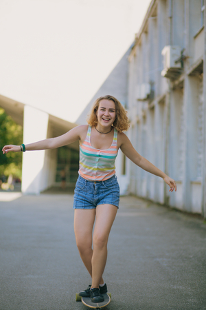Beautiful girl is skateboarding in a park. Smiling girl on the skateboard. Blond girl tries not to fall from the skateboard.の写真素材