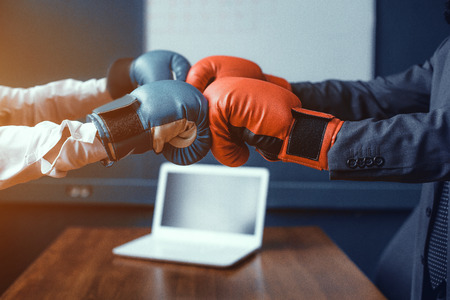 Man and woman in boxing gloves standing at table. Laptop on table. Fight of genders concept.の写真素材