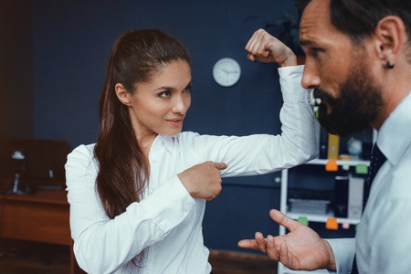 Young business woman showing muscles to her male colleague in office. Fight of genders concept.の写真素材