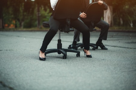 Businesspeople having racing on office chairs. Being outside. Showing good results. Fight of genders concept.の写真素材