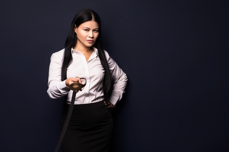 asian businesswoman with sword. isolated on dark background.の写真素材
