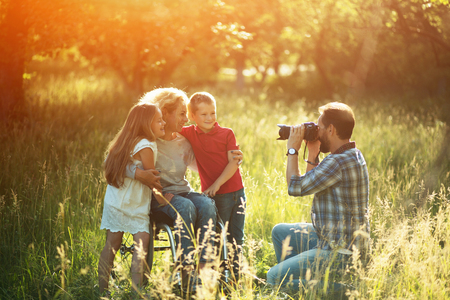 Cheerful Woman In Wheelchair With Two Cute Children Poses To Her Husband Who Is Taking Photos Of Them Having Fun.の写真素材