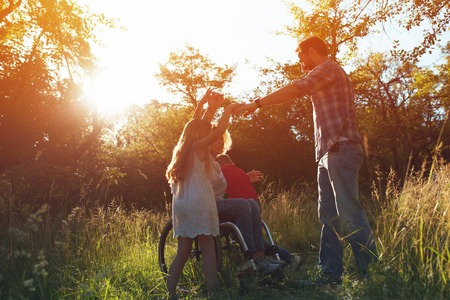 Caring Husband Reaches For The Hands Of His Kids While Wife In An Armchair Happily Laughs. Outdoorの写真素材