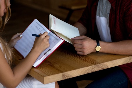 Dating Couple Preparing To Finals In Cozy Cafe. Girl Making Notes While Boy Reading Book.の写真素材