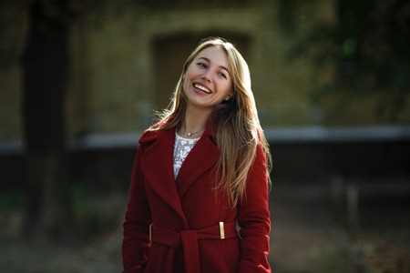 Woman In Red Coat Walking In Nature. Happy And Smiling Posing On Camera.