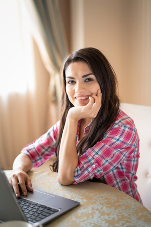 Pretty Girl Is Working On Her Laptop. Beautiful Woman Is Smiling In The Camera And Looks Very Happy Working With Her Laptop.の写真素材