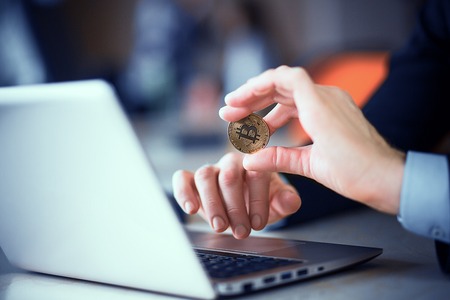 Bitcoin coin in the hand of the manager who sits at the office table and works at the computer. Gold Coin Macro Closeupの写真素材