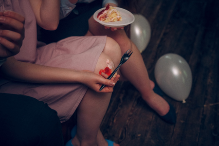 Detailed view on a girls knees with a piece of cake falling down. Womans hand with silver fork is trying to catch the falling piece of a birthday cake.の写真素材