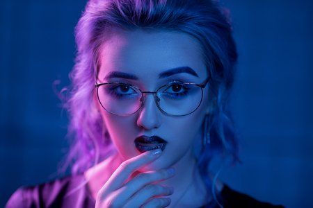 Beautiful Woman With Evening Makeup. Portrait Of Sexual Blonde Girl Wearing Glasses And Aggressive Vamp Makeup. Glamour Nightclub Makeup. Nightclub Lightning Of Bluish And Pinkish Light.の写真素材