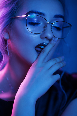 Seductive Woman In Glasses With Night Makeup Licks Her Finger. Portrait Of Beautiful Blonde Girl In Glasses Touching Her Dark Red Lips With Her Pointing Finger.の写真素材