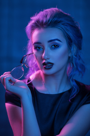 Charming Woman With Evening Makeup Holding Glasses. Close-Up Of Sexual Blonde Woman With Dark Red Lipstick And Smoky Eyes Holding A Pair Of Glasses. Nightclub Lightning.の写真素材