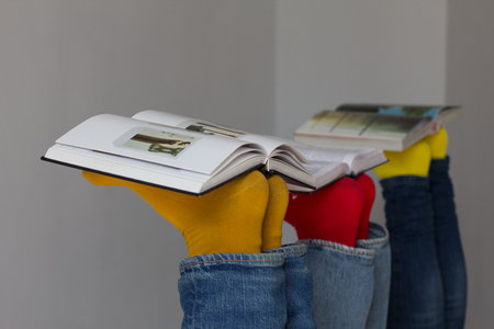 People with their feet up with books laying on top. Three open books laying on top of peoples feet who are wearing bright coloured socks.の写真素材