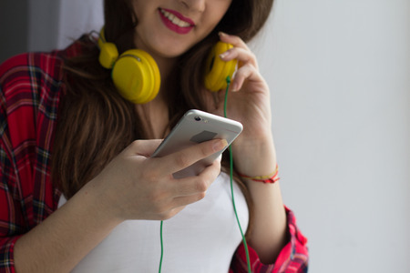 Cropped portrait of young teenager with headphones on. Young girl playing music using her smartphone and wearing yellow coloured headphones.の写真素材