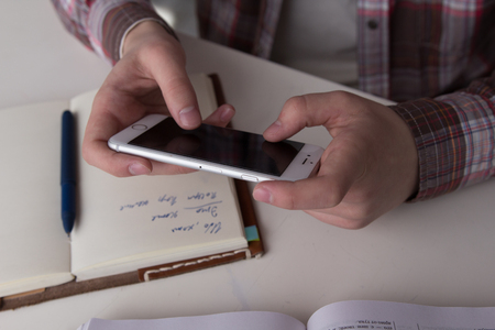 Boy holding his smartphone horizontally. Close up shot of young guy distracting himself with his phone while studying.の写真素材