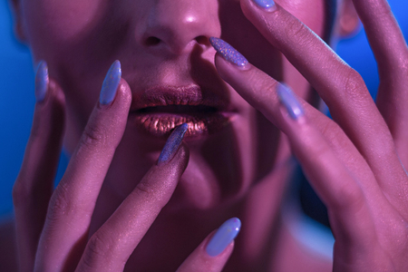 Girl model with bright makeup. Her hands with a blue manicure at her lips gold. Close Up Shoot.の写真素材