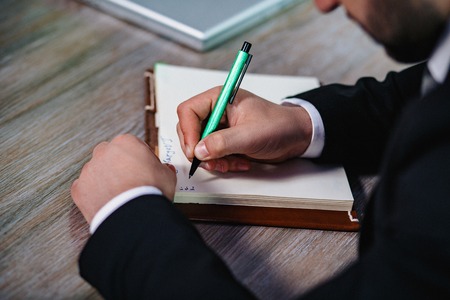 Businessmans Hand Writing Something Down In A Notebook. Close Up Of Mans Hand In Suit Writing On Notebook Or Document.の写真素材
