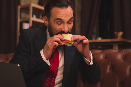 Front view image of man eating sandwich in his offce after work.の写真素材